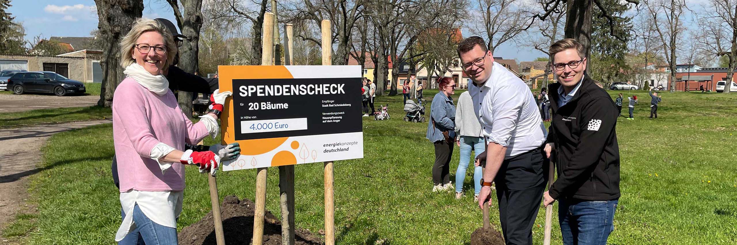 3 Personen draußen mit Schaufeln vor einem Schild auf dem Spendencheck steht