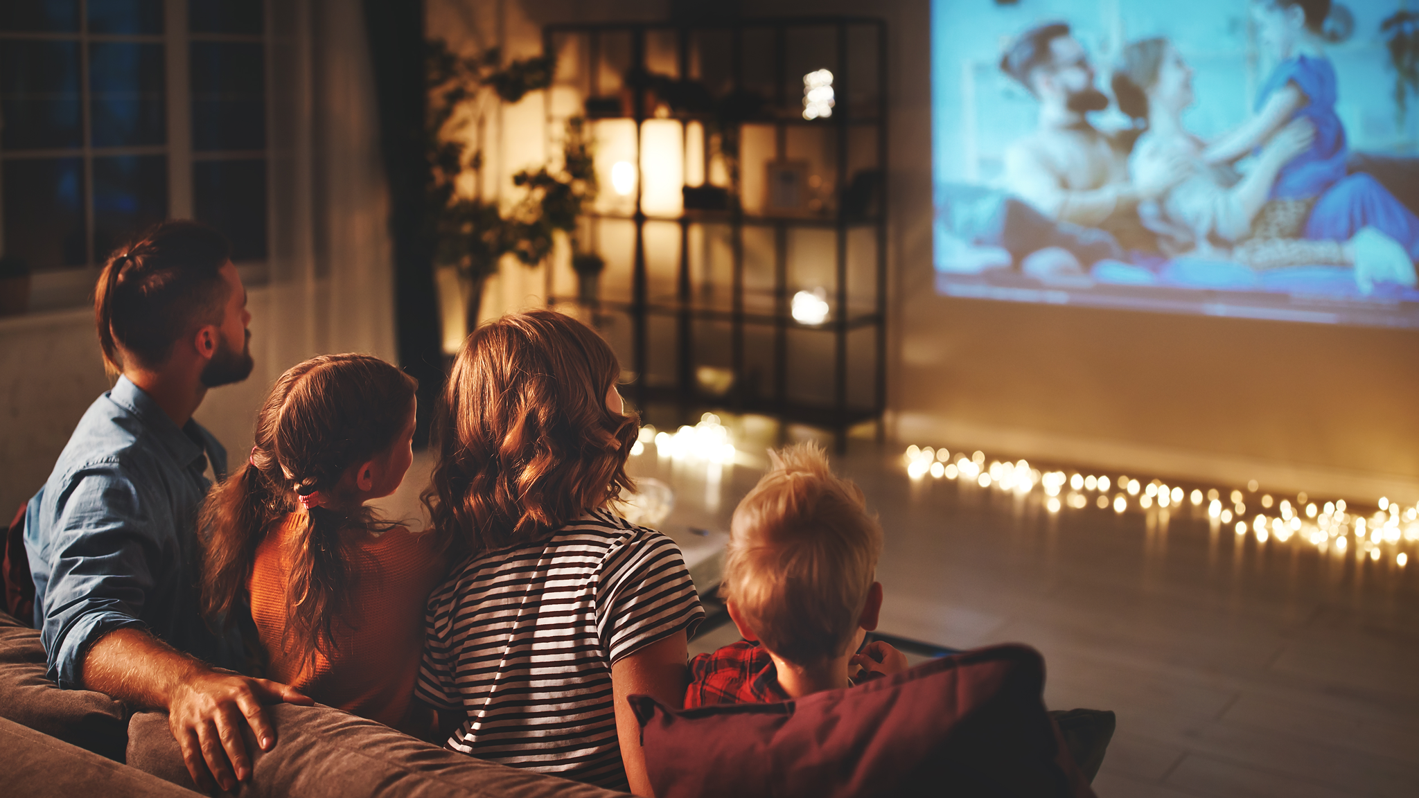 Familie sitzt auf Couch und schaut Film, Abendstimmung, Lichter sind an